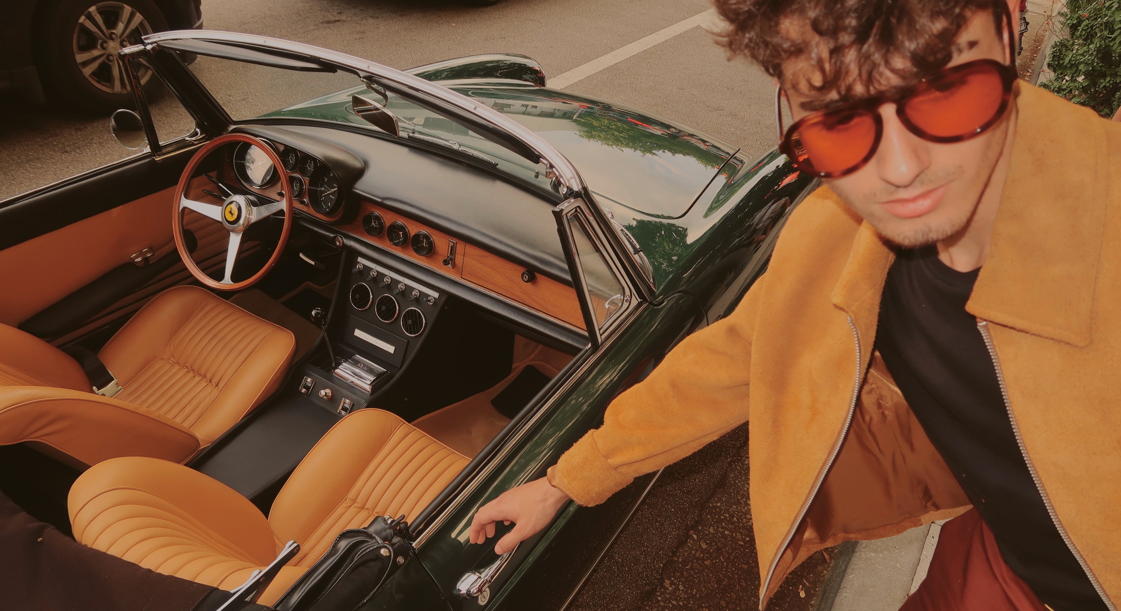 Man in a tan jacket and amber sunglasses opening the door of a classic car.
